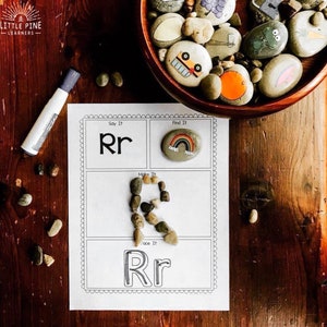 Op de afbeelding: Een printbaar werkblad om de letter R te leren. Het werkblad heeft vier secties: Zeg het, Vind het, Maak het en Traceer het. De sectie Zeg het toont de hoofdletter en kleine letter R. De sectie Vind het toont een steen met een regenboog erop geschilderd. De sectie Maak het toont de letter R gemaakt van kleine stenen. De sectie Traceer het toont een gestippelde omtrek van de letter R om te traceren.
