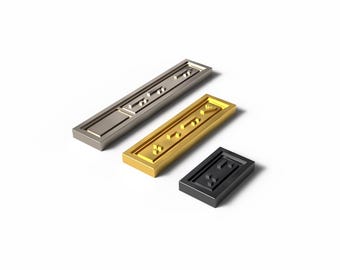 May include: Three rectangular metal decorative pieces in silver, gold, and black. Each piece has a recessed design with geometric shapes. The pieces are arranged on a white background, showcasing their metallic finish and design.