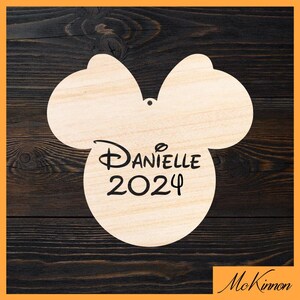 May include: A wooden ornament shaped like Mickey Mouse's head with a bow. The ornament is personalized with the name "Danielle" and the year "2024".
