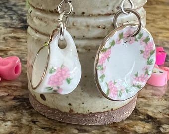 以下が含まれることがあります： ピンクの花柄のミニチュア磁器のティーカップが付いたイヤリングのペア。イヤリングはシルバーで、フック留めです。