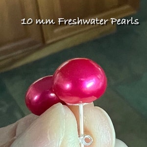 May include: A pair of pink freshwater pearl earrings, each measuring 10 mm in diameter. The pearls are a vibrant shade of pink and have a smooth, glossy finish. The earrings are attached to silver posts.