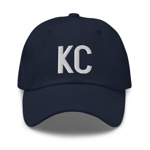 May include: A navy blue baseball cap with white embroidered lettering that says "KC".
