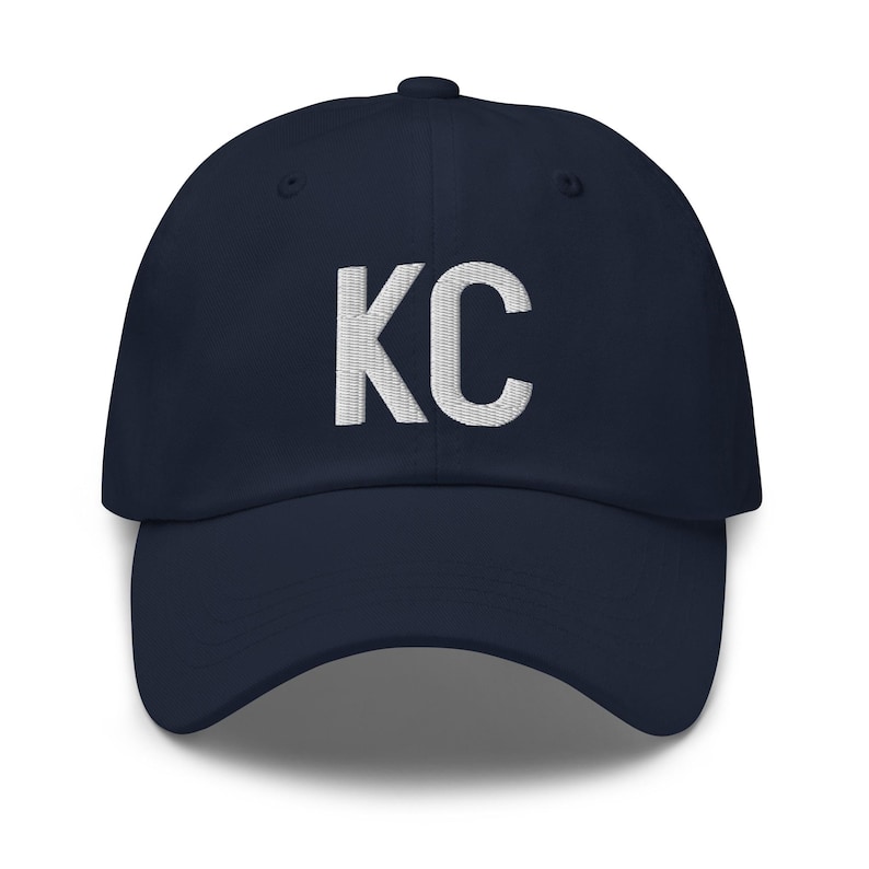 May include: A navy blue baseball cap with white embroidered lettering that says "KC".