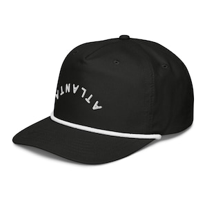 Peut inclure: Une casquette de baseball noire avec une bordure en corde blanche et le mot "ATLANTA" brodé en blanc sur le devant.