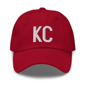May include: Red baseball cap with white embroidered text "KC" on the front.