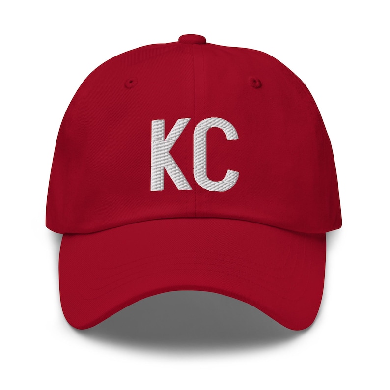 May include: Red baseball cap with white embroidered text "KC" on the front.