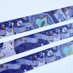 May include: Decorative washi tape featuring a repeating pattern of crowns, stars, and playing card imagery in shades of blue, gold, and white. The tape has a semi-transparent quality, with the design elements layered over a blue background.