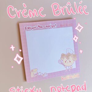 May include: Pink and white sticky notepad with a grid pattern and a cartoon chef character. The notepad says "Follow the recipe!" and "Kaiiiiichii" on the top and bottom. The notepad is on a light pink background.