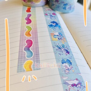 May include: Two rolls of decorative washi tape. One roll has a rainbow pattern with a wavy design. The other roll has a blue background with a cartoon character design. The text "Kaiiichii" is visible on the page.