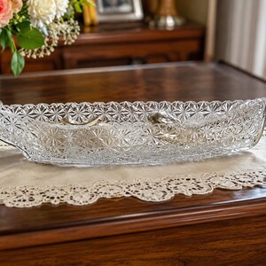 May include: A clear, elongated glass bowl featuring a detailed, repeating starburst pattern across its entire exterior surface. The vessel has a shallow, boat-like shape with scalloped edges, crafted from pressed glass with a reflective finish.