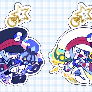 Puede incluir: Dos llaveros de personajes de dibujos animados. Un personaje lleva un gorro azul marino con una raya roja y un uniforme negro. El otro personaje lleva un gorro blanco con una raya roja y un uniforme blanco. Ambos llaveros tienen un cierre dorado en forma de estrella.