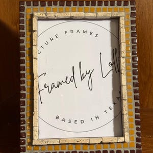 May include: A rectangular picture frame with a mosaic tile border. The frame features a mix of brown, yellow, and beige tiles. The text "PICTURE FRAMES Framed by Lollie BASED IN TEXAS" is visible within the frame.