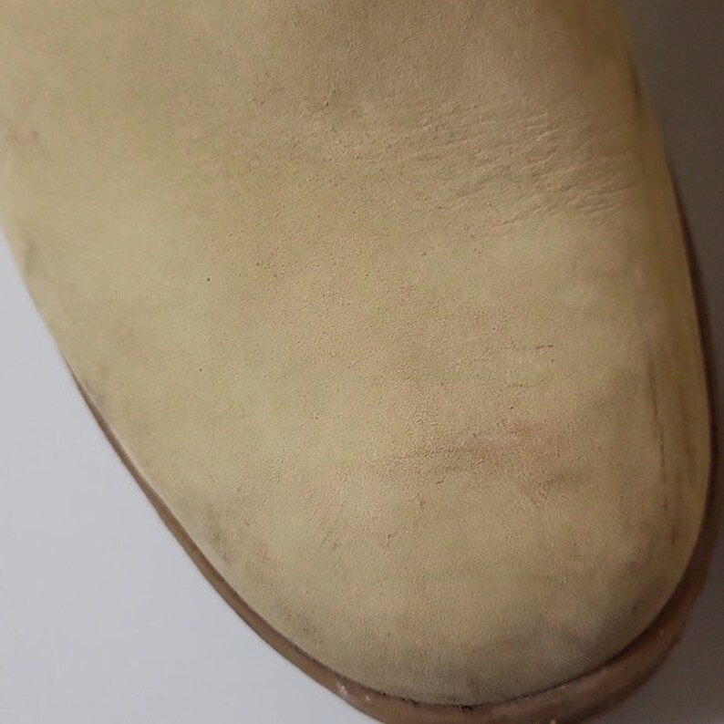Pu&ograve; includere: Primo piano della punta di uno stivale in camoscio beige chiaro. Il camoscio &egrave; leggermente usurato e ha una texture morbida.