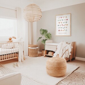 May include: A nursery room with a crib, a changing table, a wicker basket, a woven ottoman, and a framed print of the American Sign Language alphabet. The room is decorated in a neutral color palette with natural textures.