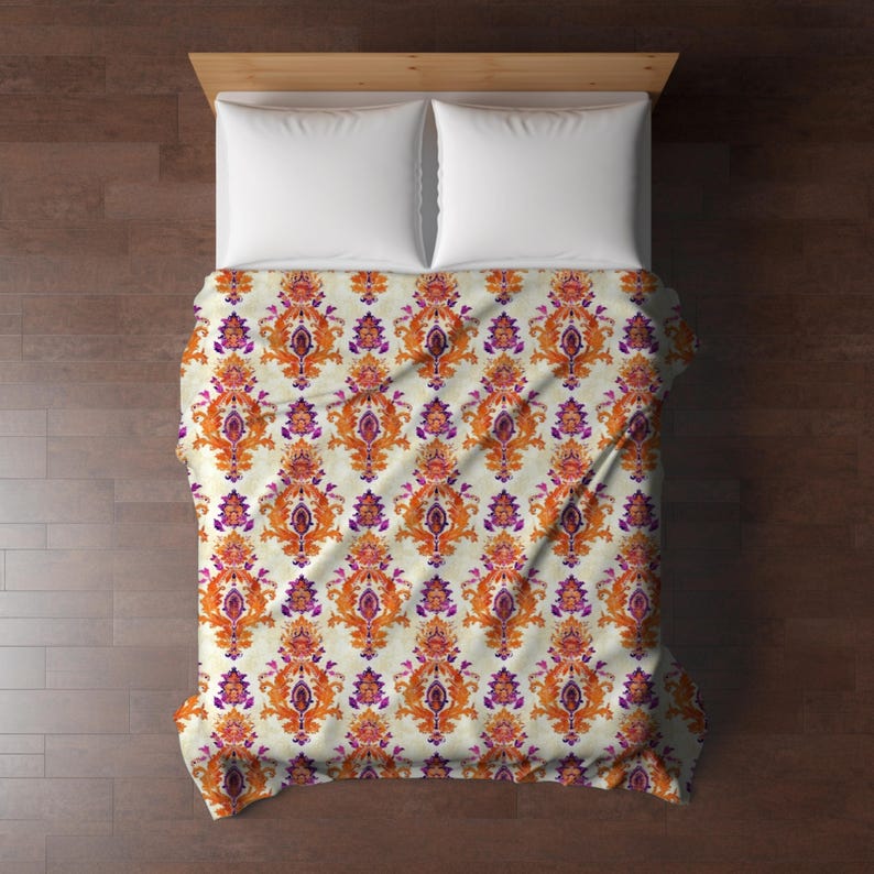 May include: A white duvet cover with a repeating pattern of orange and purple floral designs. The duvet cover is on a bed with two white pillows.
