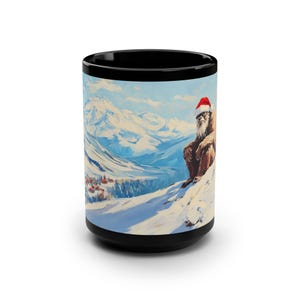 May include: A black coffee mug with a white design of a Bigfoot wearing a Santa hat and sitting on a snowy mountaintop. The background shows a snowy mountain range and a small village in the distance.