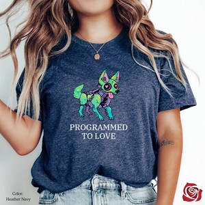 May include: A heather navy blue t-shirt featuring a colorful illustration of a robot dog with the text "Programmed to Love".