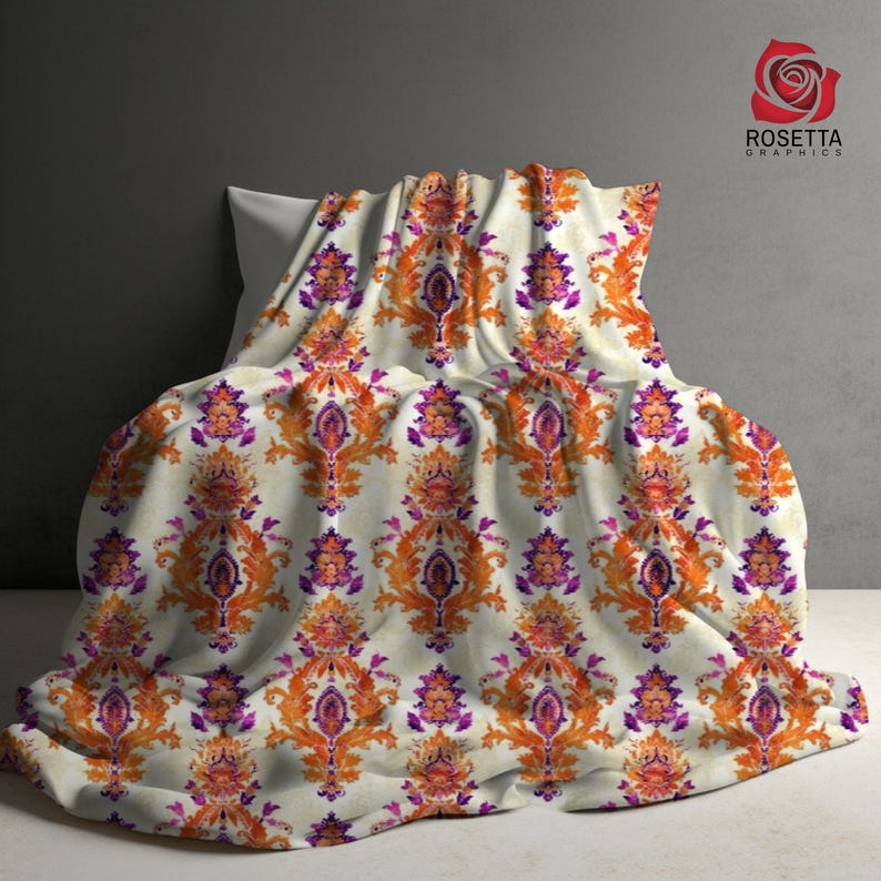 May include: A white throw blanket with a repeating pattern of orange and purple floral designs. The blanket is folded and draped over a pillow.