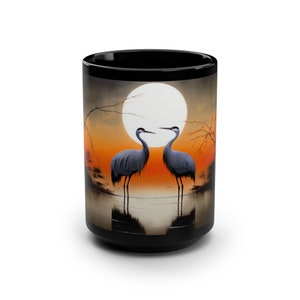May include: Black ceramic mug with a colorful image of two cranes standing in a lake with a full moon in the background.
