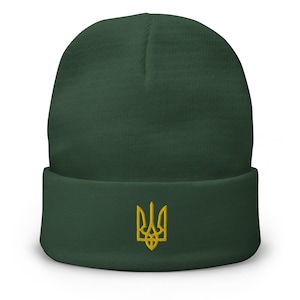 May include: A dark green beanie with a gold embroidered Ukrainian trident symbol.