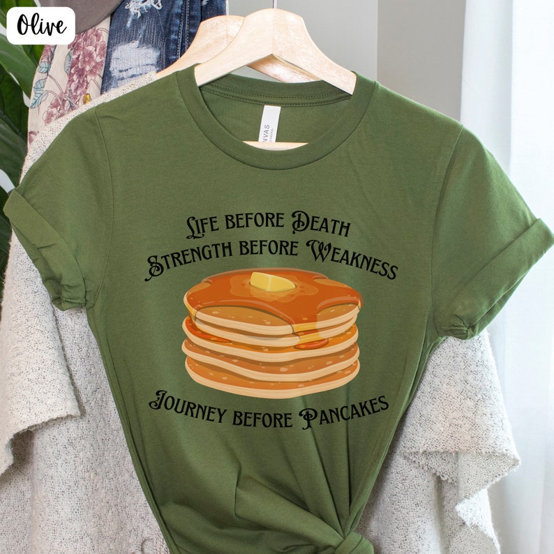 May include: Olive green t-shirt with a graphic of a stack of pancakes and the text "Life before death, strength before weakness, journey before pancakes."