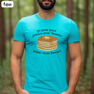 May include: A turquoise blue t-shirt with a graphic of a stack of pancakes and the text "Life before Death, Strength before Weakness, Journey before Pancakes".