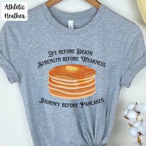 May include: A gray t-shirt with the text "Life before death, strength before weakness, journey before pancakes" and a stack of pancakes with butter and syrup.