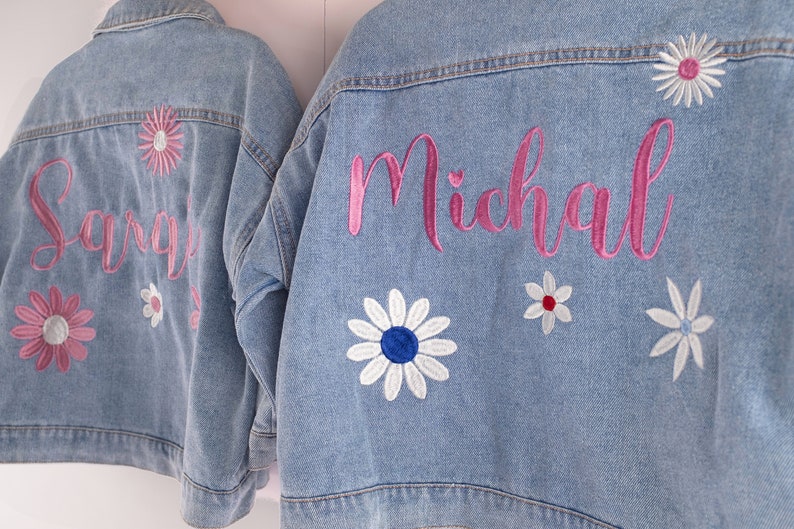 May include: Two denim jackets with embroidered flowers and names. The jacket on the left has the name "Sargis" embroidered in pink and the jacket on the right has the name "Michal" embroidered in pink.