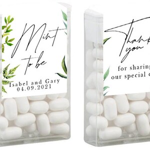 May include: Two clear plastic containers filled with white mints. One container has a label that says "Mint to be" with the date "04.09.2021" and the names "Isabel and Gary". The other container has a label that says "Thank you for sharing our special day". Both labels have green watercolour floral designs.