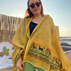 Peut inclure: Ch&acirc;le jaune moutarde avec une bordure d&eacute;corative orn&eacute;e de motifs de cerfs et d'oiseaux verts et rouille. Le ch&acirc;le est drap&eacute; sur les &eacute;paules. Le fond est un ciel clair.