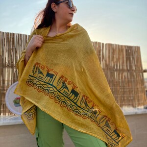 Peut inclure: Ch&acirc;le jaune moutarde avec une bordure imprim&eacute;e repr&eacute;sentant des motifs de cerfs et d'arbres en vert fonc&eacute; et rouille. Le ch&acirc;le est drap&eacute; sur les &eacute;paules, associ&eacute; &agrave; un pantalon vert.