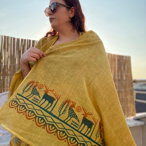 Peut inclure: &Eacute;charpe jaune moutarde avec une bordure d&eacute;corative repr&eacute;sentant des cerfs et des motifs g&eacute;om&eacute;triques en vert d'eau et rouille. L'&eacute;charpe est drap&eacute;e sur les &eacute;paules.