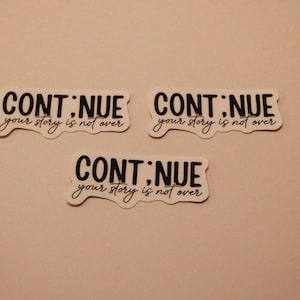 May include: Three white stickers with the words "CONTINUE" and "your story is not over" in black script. The stickers have a unique, irregular shape and are arranged on a light beige background.