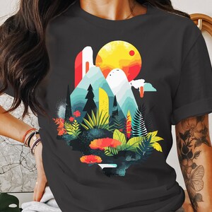 May include: A dark gray t-shirt with a colorful graphic print of a mountain landscape with a sun and trees. The graphic is in a modern, abstract style.