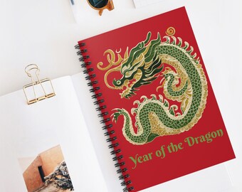 May include: A spiral-bound notebook with a red cover featuring a gold and green dragon design. The text "Year of the Dragon" is printed in green. The notebook is open, revealing blank pages.