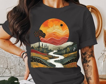 Op de afbeelding: Een donkergrijs T-shirt met een kleurrijke grafische print van een kronkelende rivier die door een landschap stroomt met een grote oranje zon en een kleine zwarte zon aan de hemel.