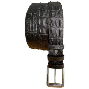 May include: A black leather belt with a textured crocodile pattern. The belt has a silver-colored buckle and a matching belt loop. The belt is made of genuine leather and is designed for everyday wear.