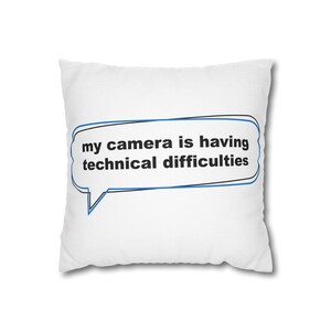 May include: A square white throw pillow featuring a blue and black outlined speech bubble graphic. Inside the speech bubble, the text reads in black lowercase letters: my camera is having technical difficulties. The pillow has a clean, simple design.