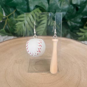 May include: A pair of baseball-themed earrings. One earring is a white baseball with red stitching, the other a miniature wooden bat. The earrings hang from silver-coloured hooks, ideal for sports enthusiasts.