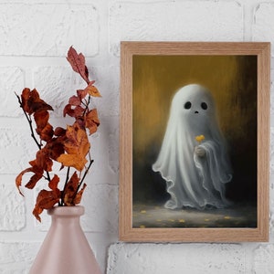 May include: A framed art print featuring a whimsical ghost holding a yellow flower. The ghost is draped in a white sheet, set against a warm, golden background. A pink vase with autumn leaves is in the foreground.