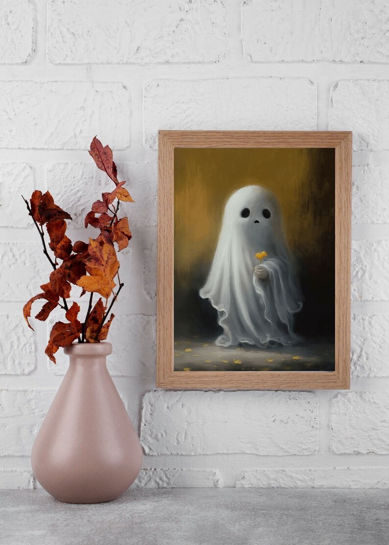 May include: A framed art print featuring a whimsical ghost holding a yellow flower. The ghost is draped in a white sheet, set against a warm, golden background. A pink vase with autumn leaves is in the foreground.