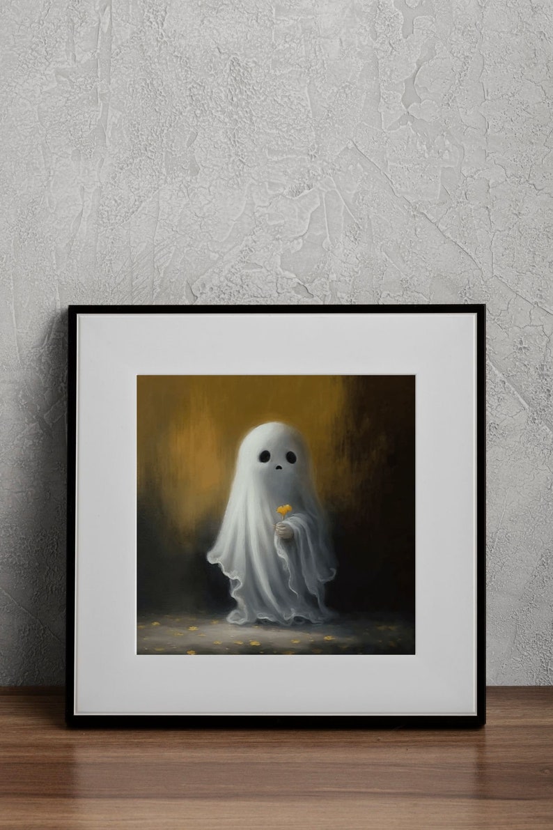May include: A framed art print featuring a whimsical ghost holding a yellow flower. The ghost is draped in a white sheet, set against a warm, golden background. The artwork is framed in a black frame and rests on a wooden surface.