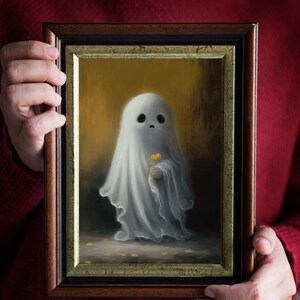 May include: A framed painting depicts a whimsical ghost holding a yellow flower. The ghost is draped in a white sheet, set against a golden background. The frame is dark brown with a gold inner border.