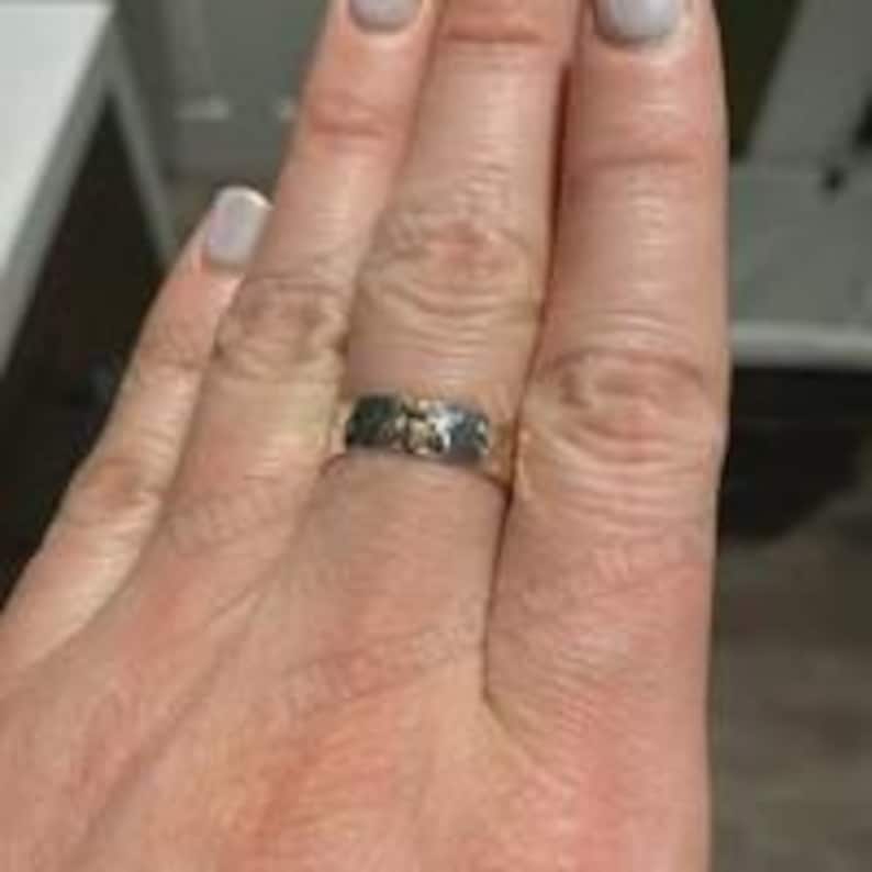 May include: A silver ring with a textured band and gold-colored accents. The ring is worn on a finger, showcasing its intricate design. The ring's details are visible, highlighting the craftsmanship.