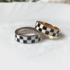 May include: Two rings with a checkerboard pattern of black and white squares. One ring is silver-toned, and the other is gold-toned. The rings are displayed on a white surface. The text "Nisha Jewellery" is visible.