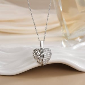 May include: A silver heart pendant necklace. The heart is split, with one half featuring an openwork design and the other half encrusted with small, sparkling stones. The necklace hangs on a delicate chain.