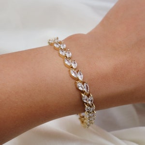 May include: A gold bracelet with a delicate design featuring a row of clear marquise-shaped stones.