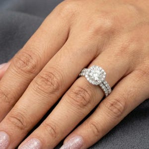 May include: A diamond engagement ring with a halo setting and a matching diamond band. The ring features a large, round-cut center stone surrounded by smaller diamonds. The band is also adorned with diamonds, creating a sparkling effect.