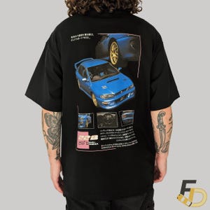 May include: Black t-shirt featuring a blue Subaru Impreza WRX graphic with Japanese text. The design includes images of the car and technical details. The shirt has short sleeves.