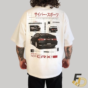 May include: White t-shirt featuring a black CRX car graphic with Japanese text and diagrams. The design includes the text "NEW CR-X" in red. The shirt has short sleeves and a relaxed fit.